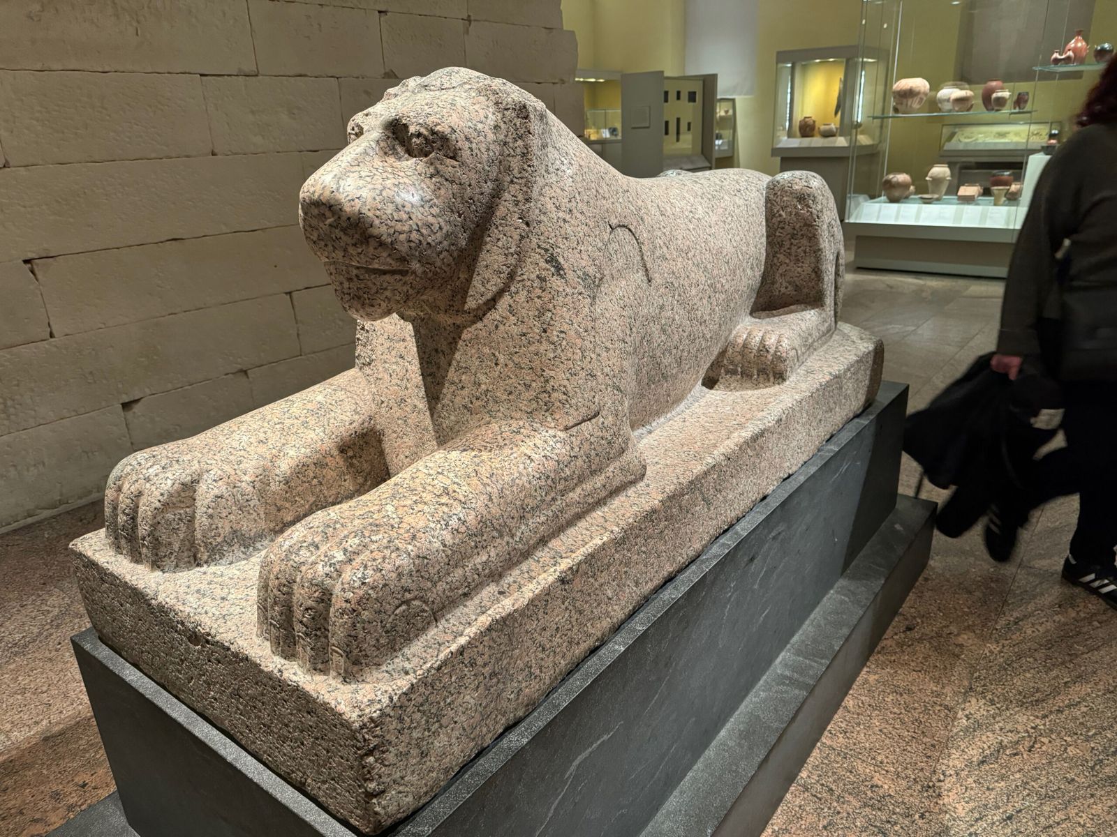 an Egyptian sculpture of a dog sitting with its paws outstretched.  It sits on a plinth and is made from marble. 